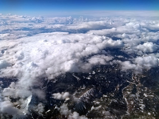 aerial view of cloud covered mountain landscape with snow visible on green hills and mountains with the curvature of the earth visible on the horizon and blue sky