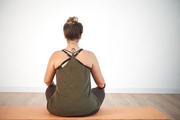 Back view of unrecognizable young woman sitting in lotus position while practicing yoga at spacious health club
