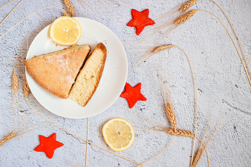 A cake with two slices of lemon on a white plate. A cup of black tea.