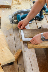 Construction of a wooden frame house - measuring the right size of the board, cutting off the saw blade with a saw, close up.