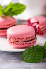 French raspberry macaroons with mint leaves on old white wooden background. Holidays food concept.