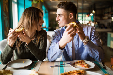 Portrait of an happy couple.They are laughing and eating pizza and having a great time in cafe.
