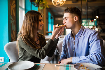 In love Couple eating pizza indoors and smiling.They are sharing pizza in a indoor cafe.