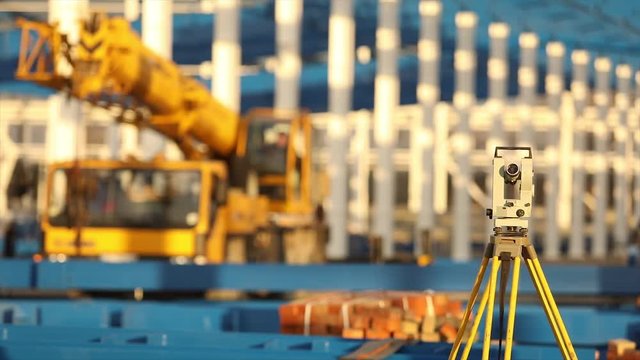 Optical Theodolite, Builders Theodolite, construction theodolite on the background of the construction of a large industrial building or warehouse, construction work