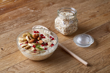 Composition with bowl of oatmeal porrige and dry oatmeal in glassware on wooden table indoors