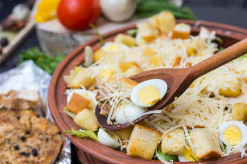 Large clay dish with tasty caesar salad with a wooden spoon in it