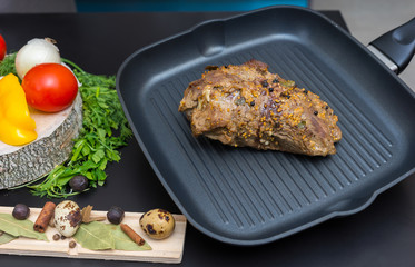 Prepared marinated meat on a grill pan next to vegetables on a wooden board