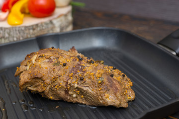 Close up of prepared meat on a grill pan next to vegetables on wooden desk