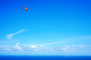 Fototapeta na wymiar Paragliding over the ocean on the island of Bali. The blue sky shimmers with the blue ocean. The parasutists fly high above the precipice like birds. Aerial view with copy space