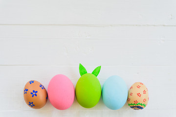 Happy easter! Row Colorful Easter eggs with colorful paper flowers on white wooden background.