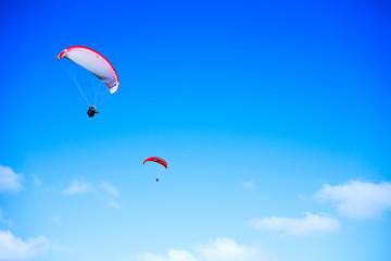 Fototapeta na wymiar Paragliding over the ocean on the island of Bali. The blue sky shimmers with the blue ocean. The parasutists fly high above the precipice like birds. Aerial view with copy space