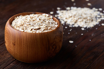 Oat flakes in bowl and wooden spoon isolated on wooden background, close-up, top view, selective focus.