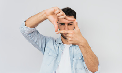 Studio portrait of handsome bearded male is looking through a frame formed by his hands. Serious...