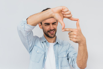 Portrait of handsome bearded happy male is looking through a frame formed by his hands. Attractive...