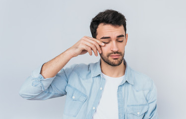 Portrait of bored sleepy bearded male after long overwork on new project, wearing blue shirt isolated on white studio background with copy space for advertising text. People and overwork concept.