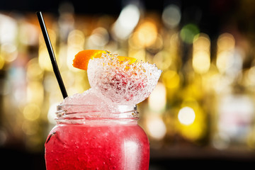 Closeup cold tasty cocltail jar decorated with orange and frappe at bar counter background.