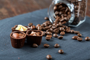 Side view of overturned glass jar with coffee beans and chocolate candies on wooden background,...