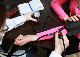 Doctor with glasses measures a blood pressure of the patient