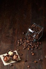 Side view of overturned glass jar with coffee beans and chocolate candies on wooden background, selective focus