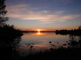 Karelia sunset with dark black silhouettes of forest with a clear reflection in water 