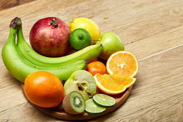 Ripe fresh fruits in a wooden plate on a light wooden background, selective focus, close-up, top view