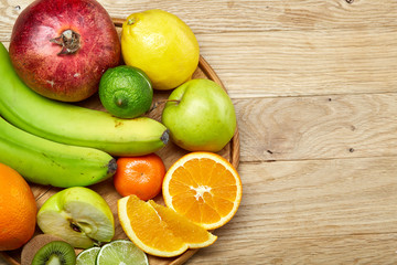 Ripe fresh fruits in a wooden plate on a light wooden background, selective focus, close-up, top view