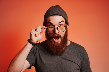 Amazed bearded hipster man touching eyeglasses and looking at the camera with surprised face...
