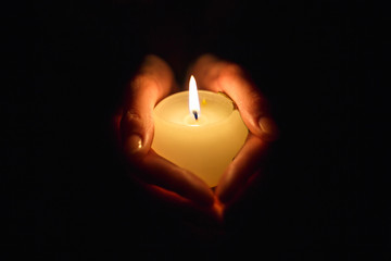 burning candle in the hands of a praying girl on a black background