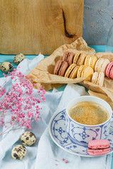 Macaroons and coffee. Blue, rose and baige colors. Wooden table. Macaroons in the box, coffee in white porcelain cup.