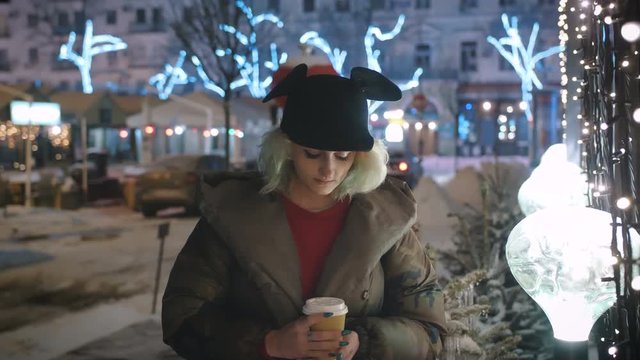 Portrait of young funky woman outdoor in wintertime at night drinking coffee
