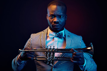 Neon portrait of handsome black jazzman in plaid jacket with floral bow tie with trumpet in his hands. Orange and blue studio light © monchak