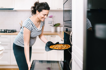 Beautiful pregnant woman in home kitchen preparing pizza and baking