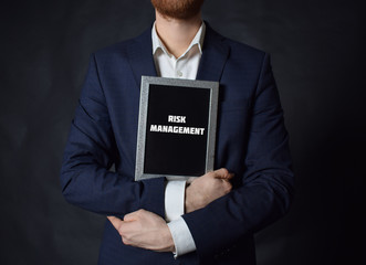 In the hands of a businessman a frame with the inscription:RISK MANAGEMENT