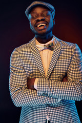 Studio neon portrait of handsome black jazzman with funny smiling face in white shirt and plaid jacket with floral bow tie and vintage cap