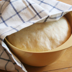 Bread dough rising in a yellow plastic bowl on wooden table