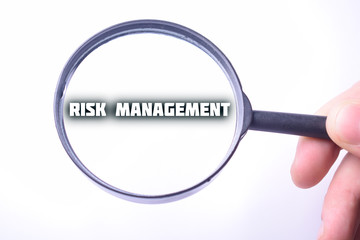 Businessman looking at a magnifying glass word:RISK MANAGEMENT