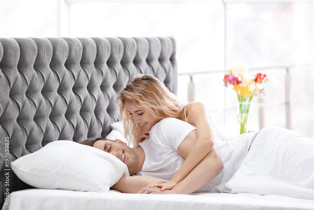 Poster lovely young woman hugging her boyfriend in bed at home