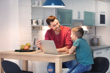 Little boy and his dad using laptop at home