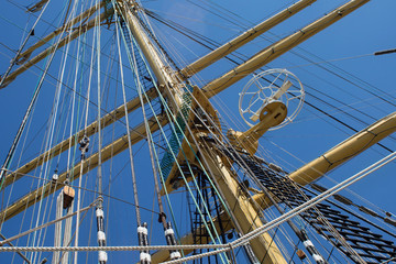 Masts of a sailing ship with the lowered sails with blue sky on the background.