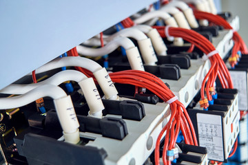 A number of magnetic starters and connected electrical wires in the electrical Cabinet. Cables with tips and digital marking. Red wires are assembled into a bundle of plastic ties.