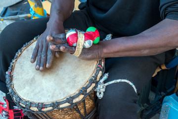 Close-up of hands of a black man playing a traditional drum.