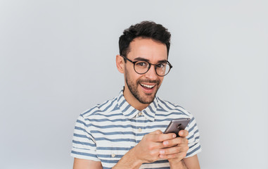 Portrait of happy handsome surprised male wearing striped shirt and reound spectalces, using smart phone for texting messages having pleasant smile showing white teeth, had amazed face for good news.