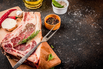 Raw beef marbled meat striplon rib eye steak with spices, herbs, dark background, on cuting board, copy space