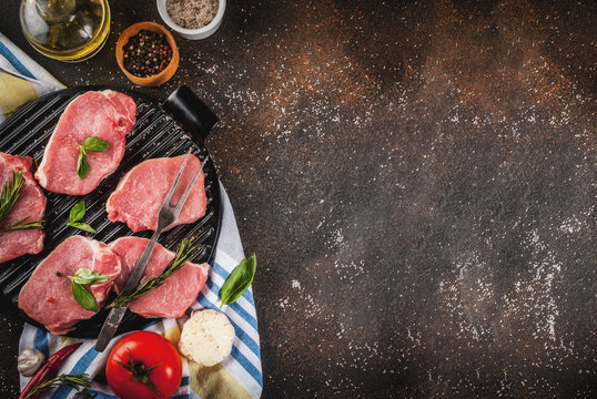 Raw meat, pork steaks with spices, herbs, olive oil, dark background on grill pan, top view, copy space