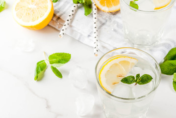Summer refreshing drinks, mojito or lemonade with fresh mint, slices of lemon, ice, on a light background. copy space