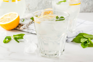 Summer refreshing drinks, mojito or lemonade with fresh mint, slices of lemon, ice, on a light background. copy space