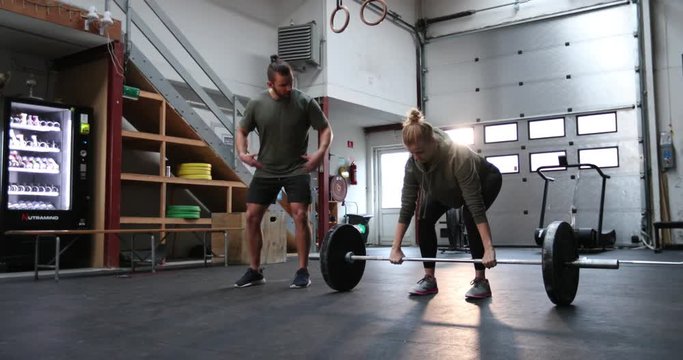 Fit young woman lifting weights on a barbell with a partner coaching her during a workout session in a gym