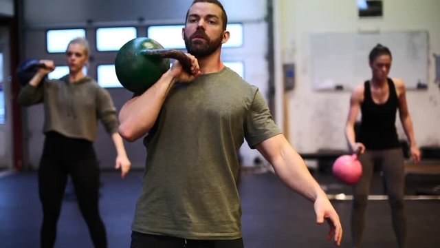 Fit young man in sportswear swinging a dumbbell during a workout class with a group of people in a gym