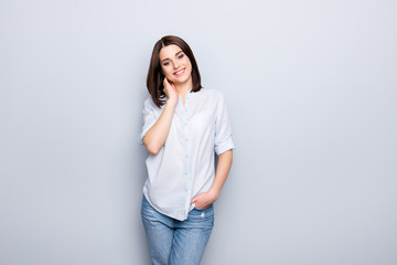 Portrait of trendy, cheerful, modern girl in denim outfit, holding hands in pocket of jeans and touching her neck, looking at camera, having short hair, isolated on grey background