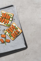 healthy sandwiches with roasted baby carrots and arugula on baking paper on grey